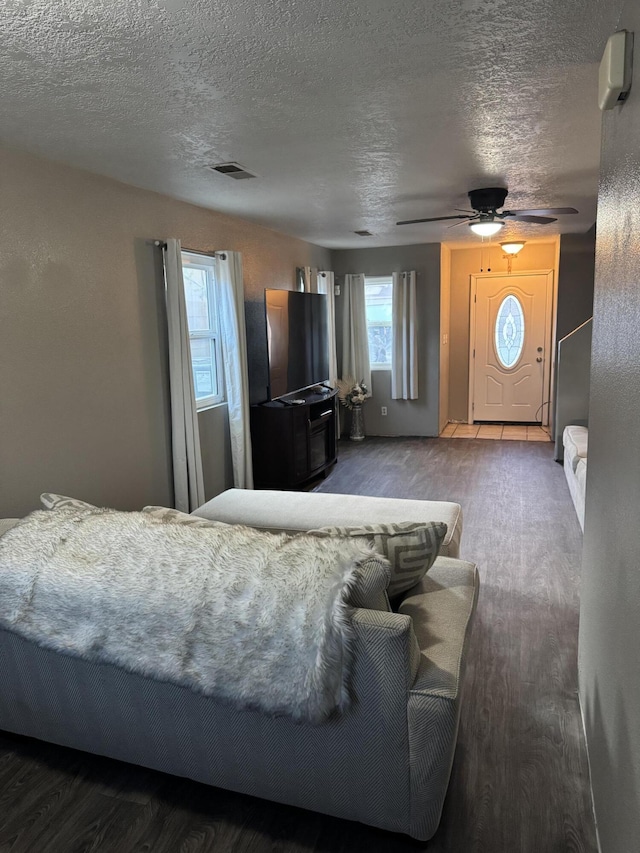 bedroom featuring ceiling fan, a textured ceiling, visible vents, and wood finished floors