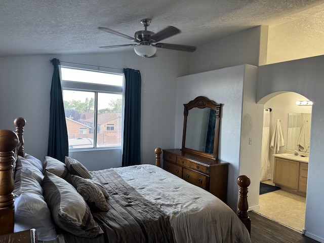 bedroom featuring arched walkways, a textured ceiling, wood finished floors, and vaulted ceiling