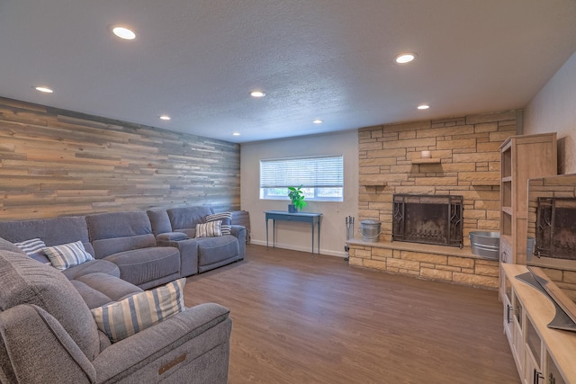 living area with wood finished floors, baseboards, a stone fireplace, recessed lighting, and a textured ceiling