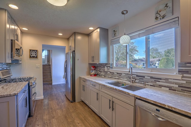 kitchen with pendant lighting, tasteful backsplash, wood finished floors, a sink, and stainless steel appliances