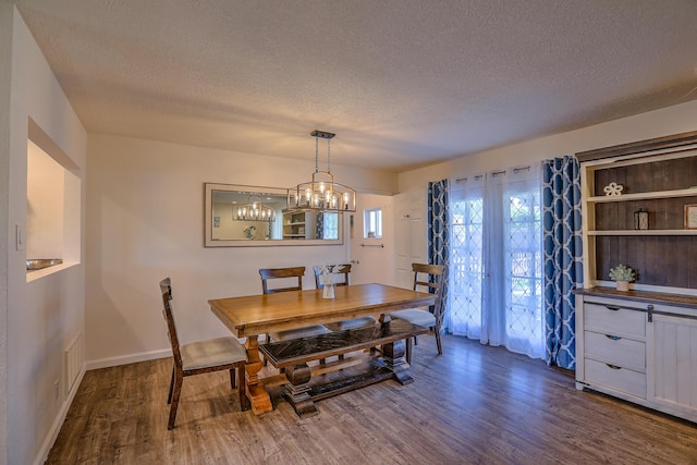 dining space with a textured ceiling, a chandelier, baseboards, and dark wood-type flooring
