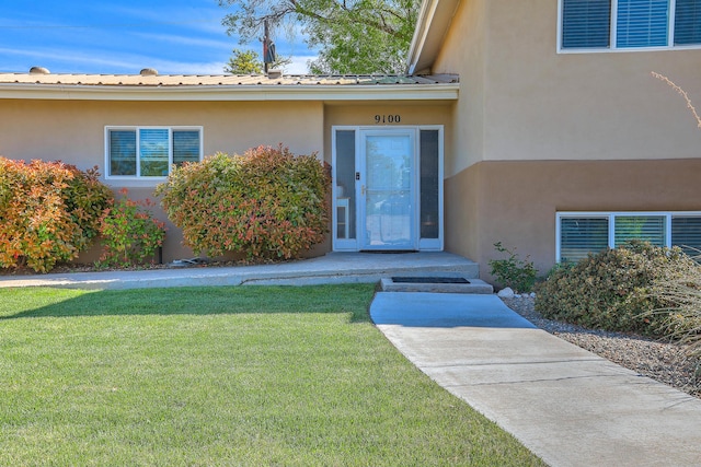 doorway to property featuring a lawn, stucco siding, and metal roof