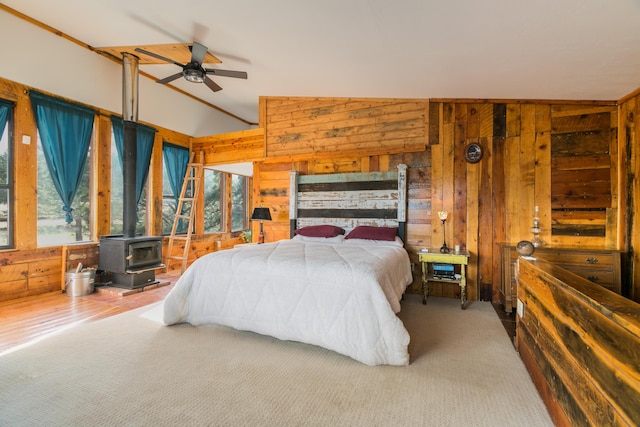 carpeted bedroom with vaulted ceiling, a wood stove, and wood walls