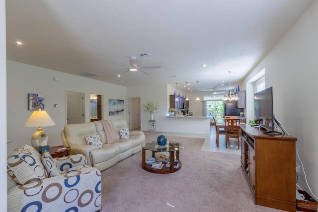 living room with visible vents, ceiling fan with notable chandelier, and light colored carpet