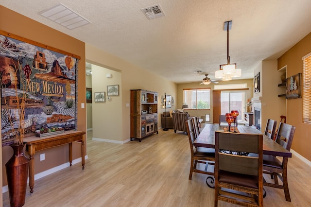 dining space featuring a textured ceiling, a ceiling fan, baseboards, light wood-type flooring, and visible vents