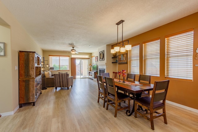 dining area with baseboards, a fireplace, light wood-type flooring, and a textured ceiling