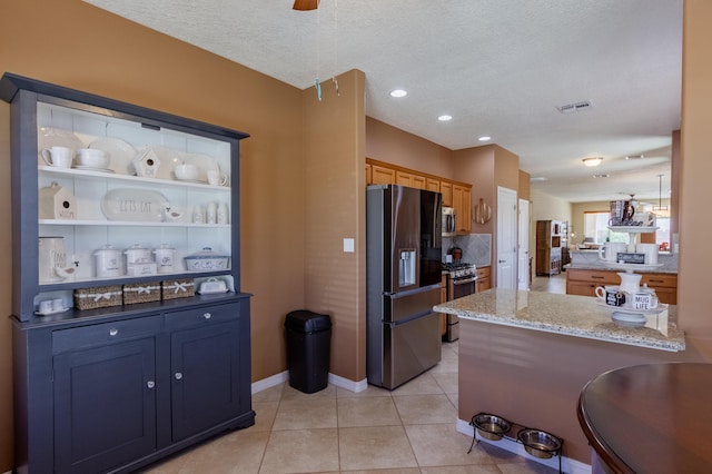 kitchen with light stone countertops, a textured ceiling, stainless steel appliances, a peninsula, and visible vents