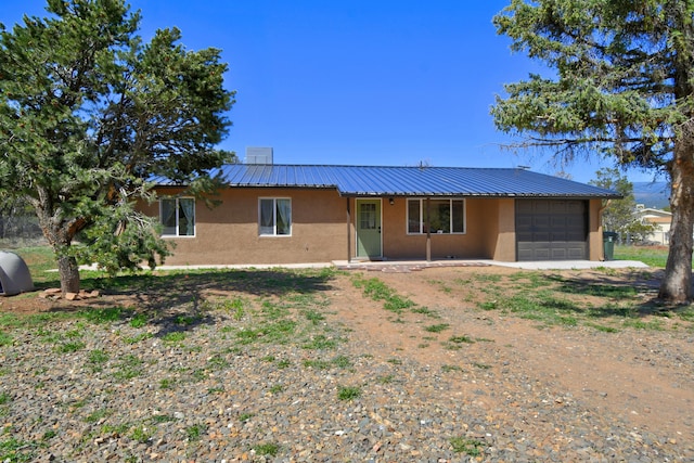 ranch-style home featuring an attached garage, stucco siding, a porch, driveway, and metal roof
