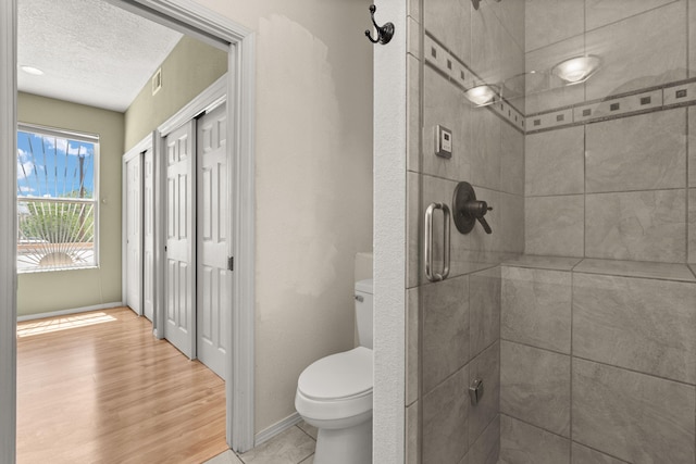 bathroom with a textured ceiling, visible vents, a tile shower, baseboards, and toilet