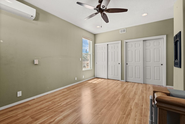unfurnished bedroom with visible vents, a wall mounted air conditioner, baseboards, two closets, and light wood-style flooring