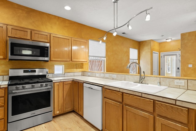 kitchen featuring a sink, tile counters, light wood-style flooring, stainless steel appliances, and a peninsula
