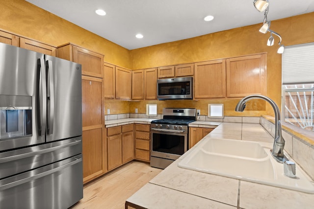 kitchen with brown cabinetry, a sink, light wood finished floors, and stainless steel appliances
