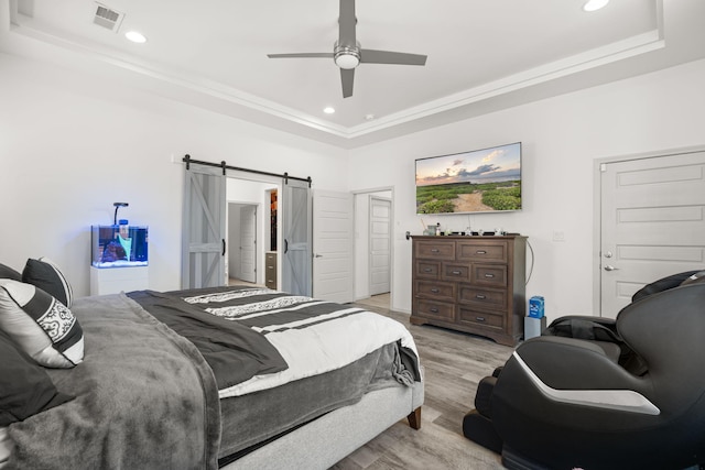 bedroom featuring visible vents, a barn door, a raised ceiling, and light wood finished floors