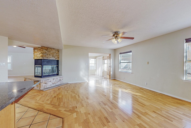 unfurnished living room with baseboards, ceiling fan, a textured ceiling, and wood finished floors