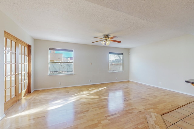 spare room featuring baseboards, a ceiling fan, light wood finished floors, and a textured ceiling