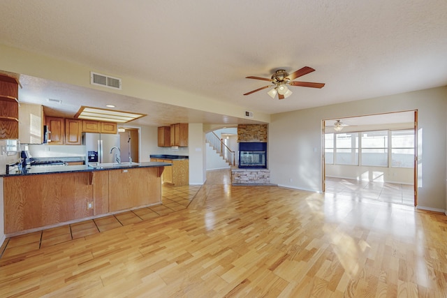 kitchen with dark countertops, a peninsula, open floor plan, stainless steel refrigerator with ice dispenser, and visible vents