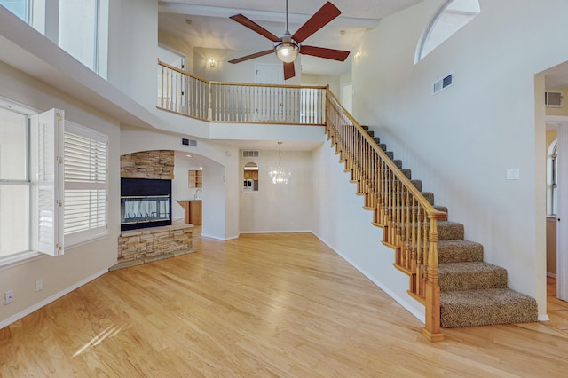 unfurnished living room with ceiling fan with notable chandelier, stairs, wood finished floors, a towering ceiling, and visible vents