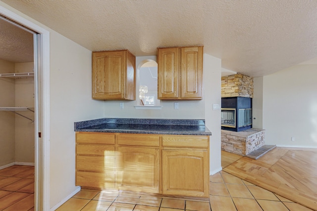 kitchen featuring baseboards, a textured ceiling, light tile patterned floors, and dark countertops