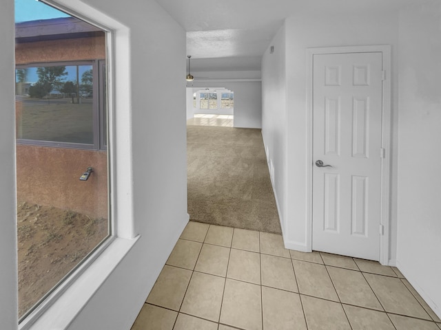 hallway with light tile patterned floors, baseboards, and light carpet