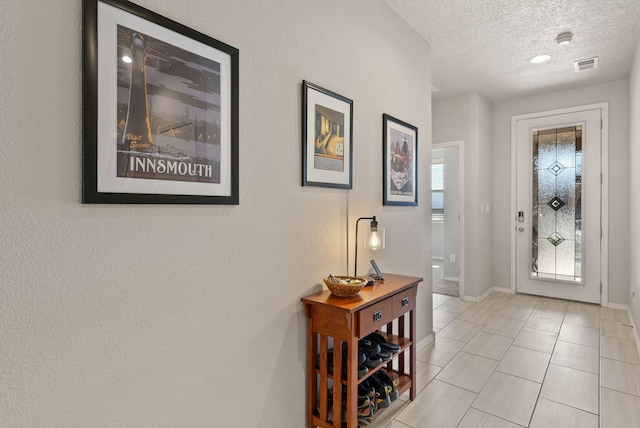 entryway featuring light tile patterned floors, baseboards, a textured ceiling, and visible vents
