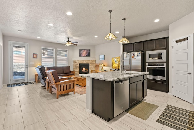 kitchen with a ceiling fan, a textured ceiling, a stone fireplace, appliances with stainless steel finishes, and a sink
