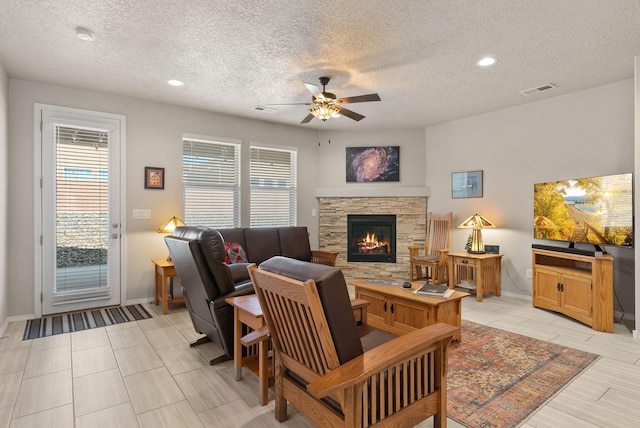 living room featuring baseboards, ceiling fan, a stone fireplace, and a textured ceiling