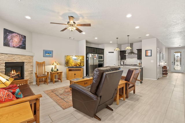 living room featuring a stone fireplace, recessed lighting, a textured ceiling, and ceiling fan