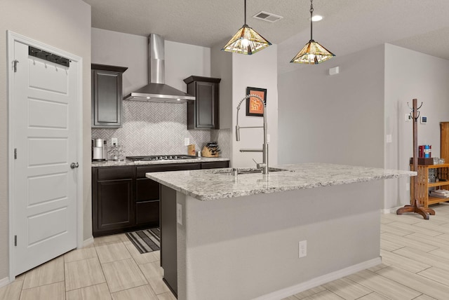 kitchen featuring visible vents, stainless steel gas cooktop, wall chimney range hood, a sink, and backsplash