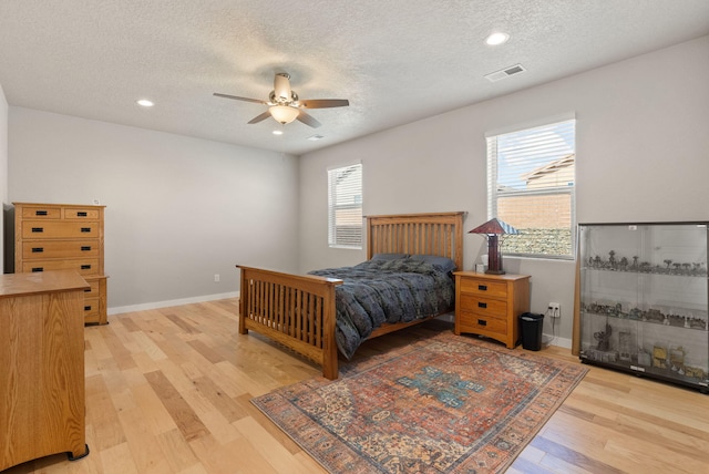 bedroom with visible vents, baseboards, a textured ceiling, a ceiling fan, and light wood-style flooring