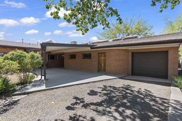 view of front of house with an attached carport, brick siding, an attached garage, and gravel driveway