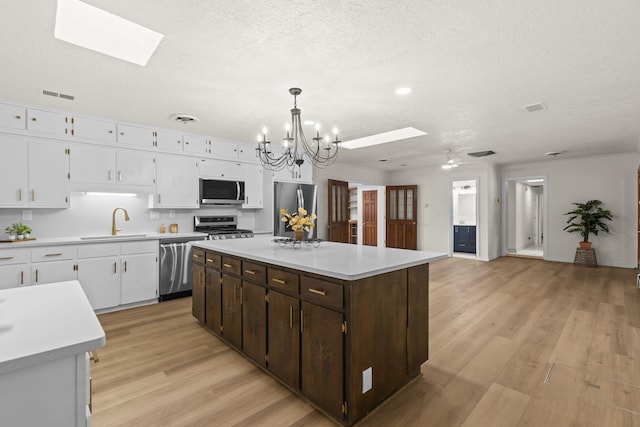 kitchen featuring light countertops, white cabinetry, a sink, a skylight, and stainless steel appliances