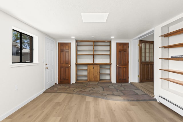 interior space featuring baseboards, light wood finished floors, baseboard heating, and a skylight