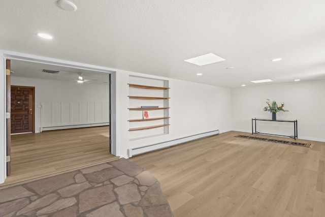 spare room featuring baseboard heating, light wood-style floors, a baseboard radiator, a skylight, and visible vents