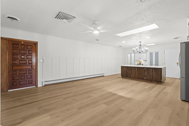 interior space with visible vents, ceiling fan with notable chandelier, baseboard heating, and a skylight