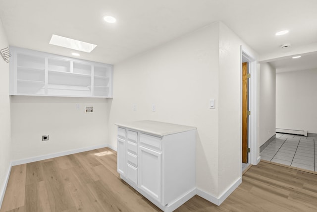 interior space with a skylight, baseboards, a baseboard heating unit, and light wood-style flooring