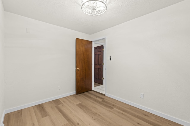 empty room with light wood-style floors, baseboards, an inviting chandelier, and a textured ceiling