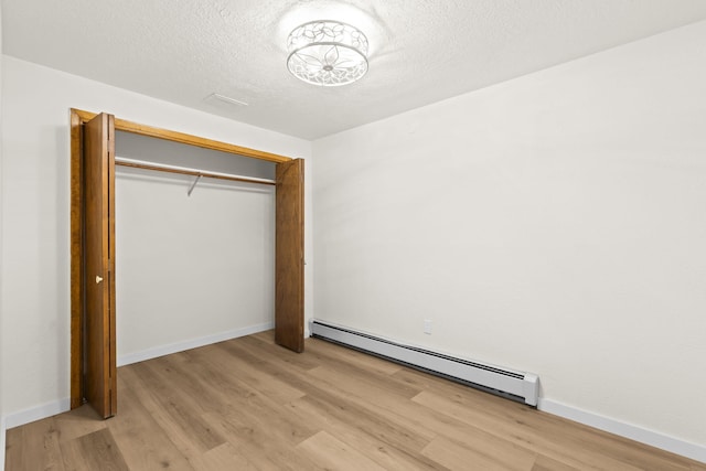 unfurnished bedroom with light wood-type flooring, baseboards, a textured ceiling, and a baseboard heating unit