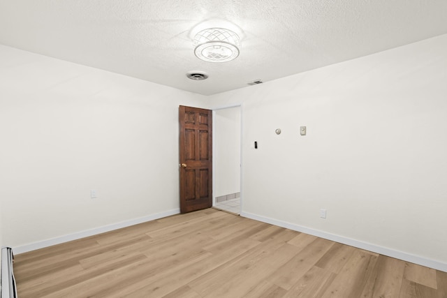 empty room with baseboards, a textured ceiling, visible vents, and light wood-style flooring