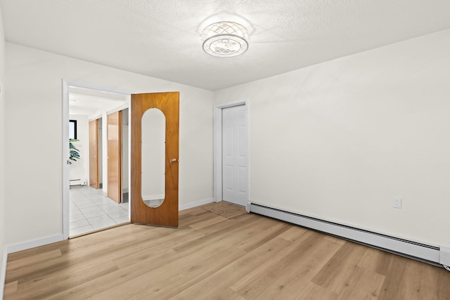 spare room with a textured ceiling, baseboards, baseboard heating, and light wood-style flooring