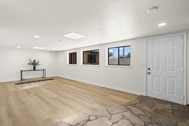 foyer entrance with light wood-style floors, a textured ceiling, recessed lighting, baseboards, and a skylight