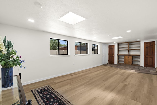 unfurnished living room featuring a textured ceiling, a skylight, baseboards, light wood-style floors, and recessed lighting
