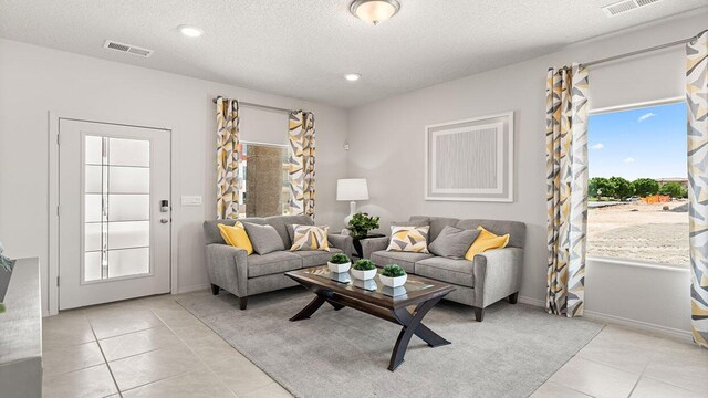 living area featuring visible vents, baseboards, a textured ceiling, and light tile patterned floors