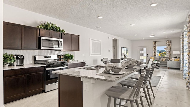 kitchen featuring a kitchen island with sink, a sink, a breakfast bar, stainless steel appliances, and light tile patterned flooring