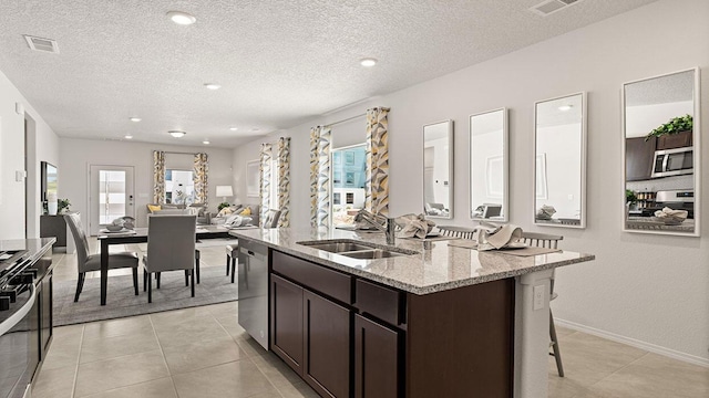 kitchen featuring visible vents, dark brown cabinetry, a kitchen island with sink, a sink, and appliances with stainless steel finishes