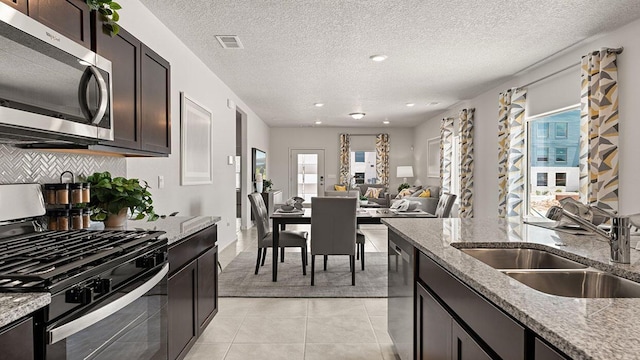 kitchen featuring visible vents, light tile patterned flooring, light stone countertops, a sink, and appliances with stainless steel finishes