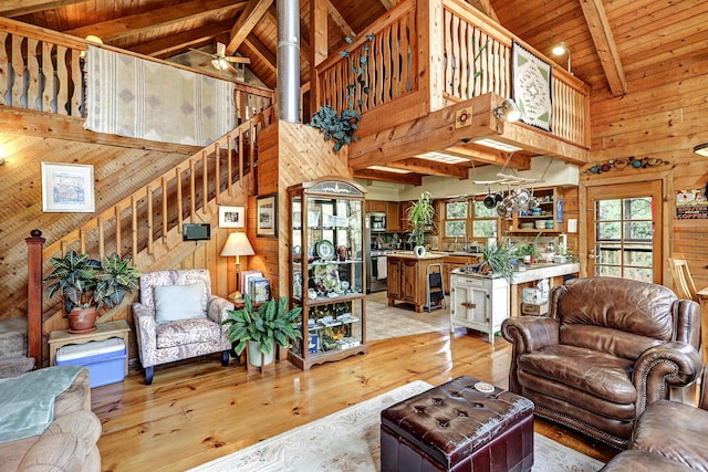 living area featuring high vaulted ceiling, wood walls, light wood-style flooring, and stairs