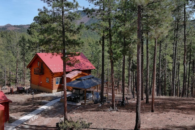 exterior space featuring a forest view, log siding, and metal roof