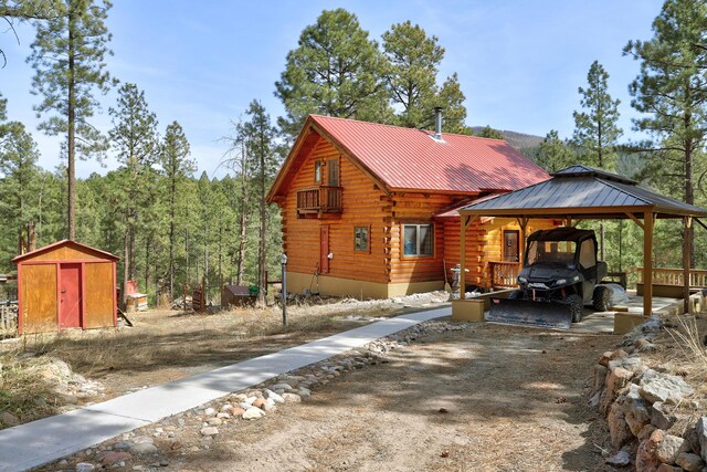 view of side of property with driveway, a carport, log exterior, an outdoor structure, and a storage unit