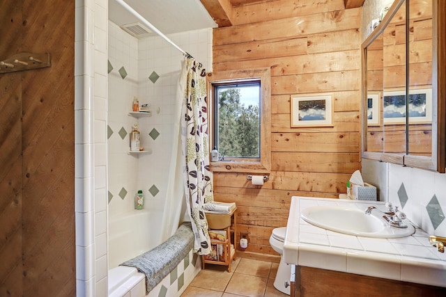 bathroom featuring wood walls, vanity, tile patterned floors, toilet, and tiled shower / bath combo
