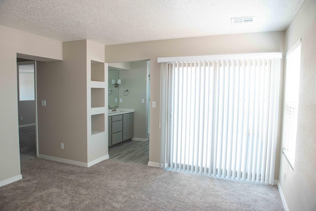 unfurnished living room with baseboards, carpet flooring, a textured ceiling, and visible vents